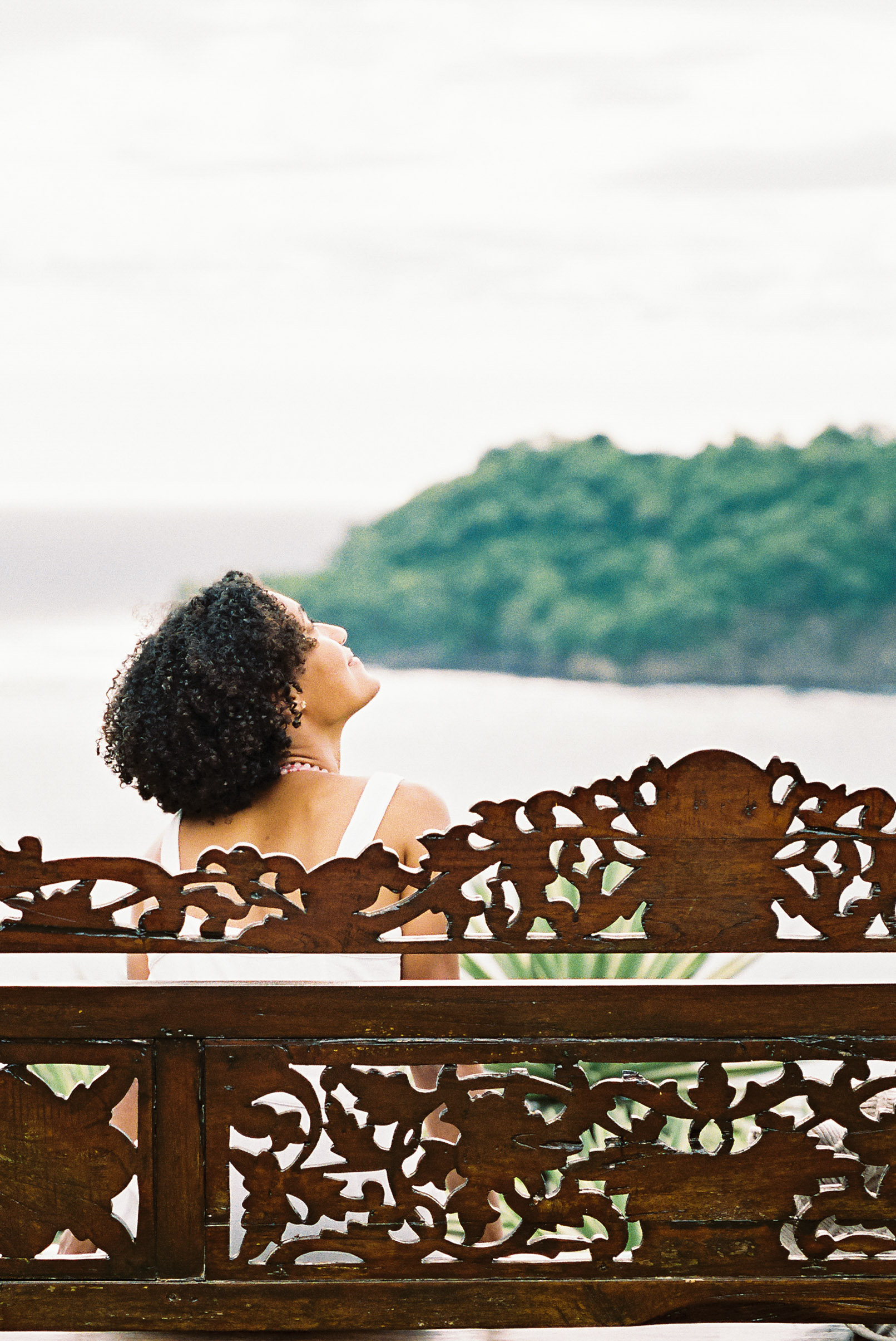 Asia Pimentel looking up at the sky from a carved wooden bench by the sea