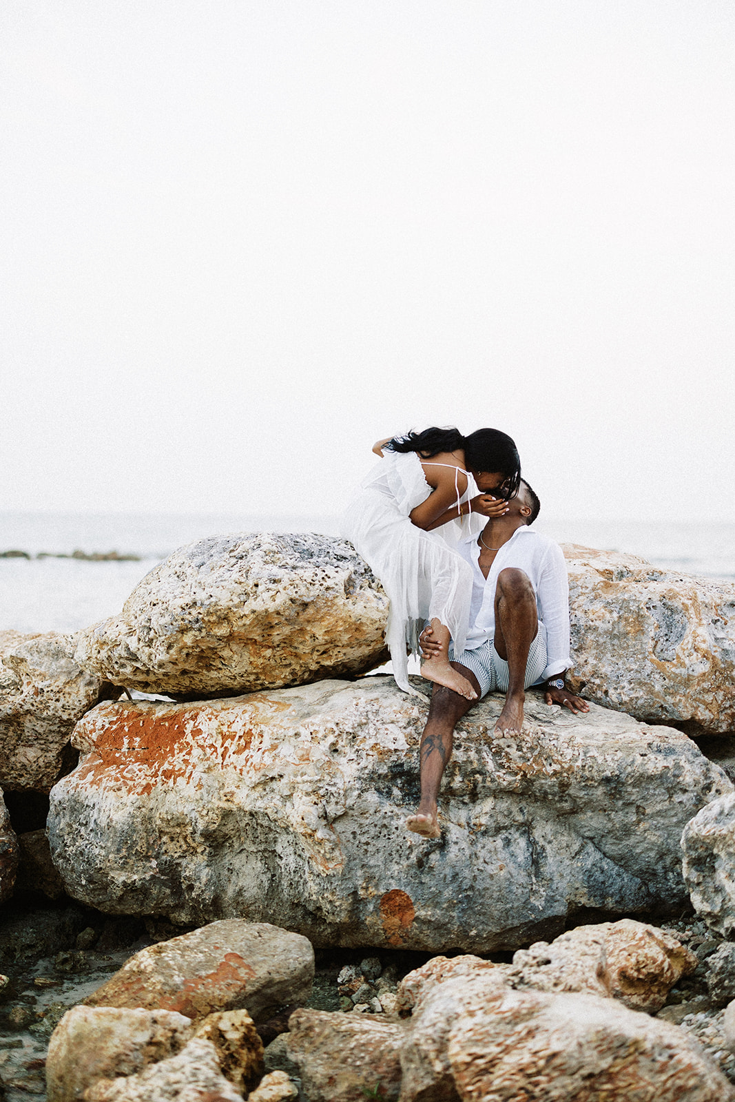 Couple kissing and sitting together on rocks during portrait session at Casa de Campo, Dominican Republic