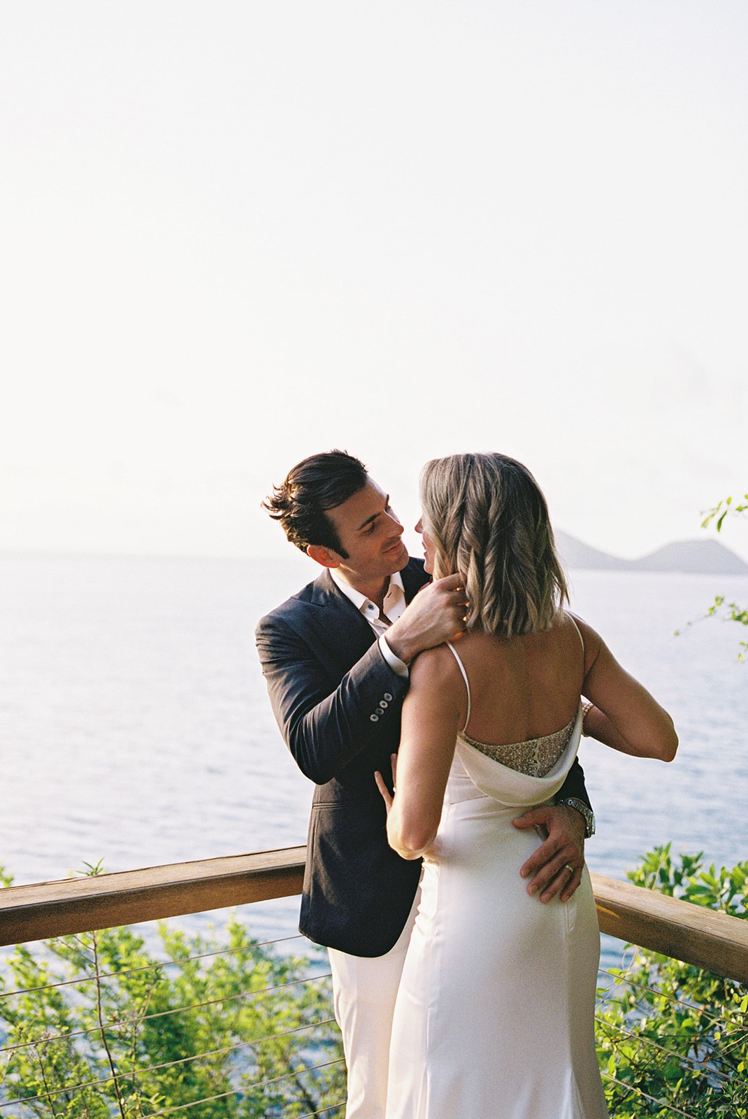 Aaron and Elizabeth embracing on the cliffside terrace, ocean and islands behind them